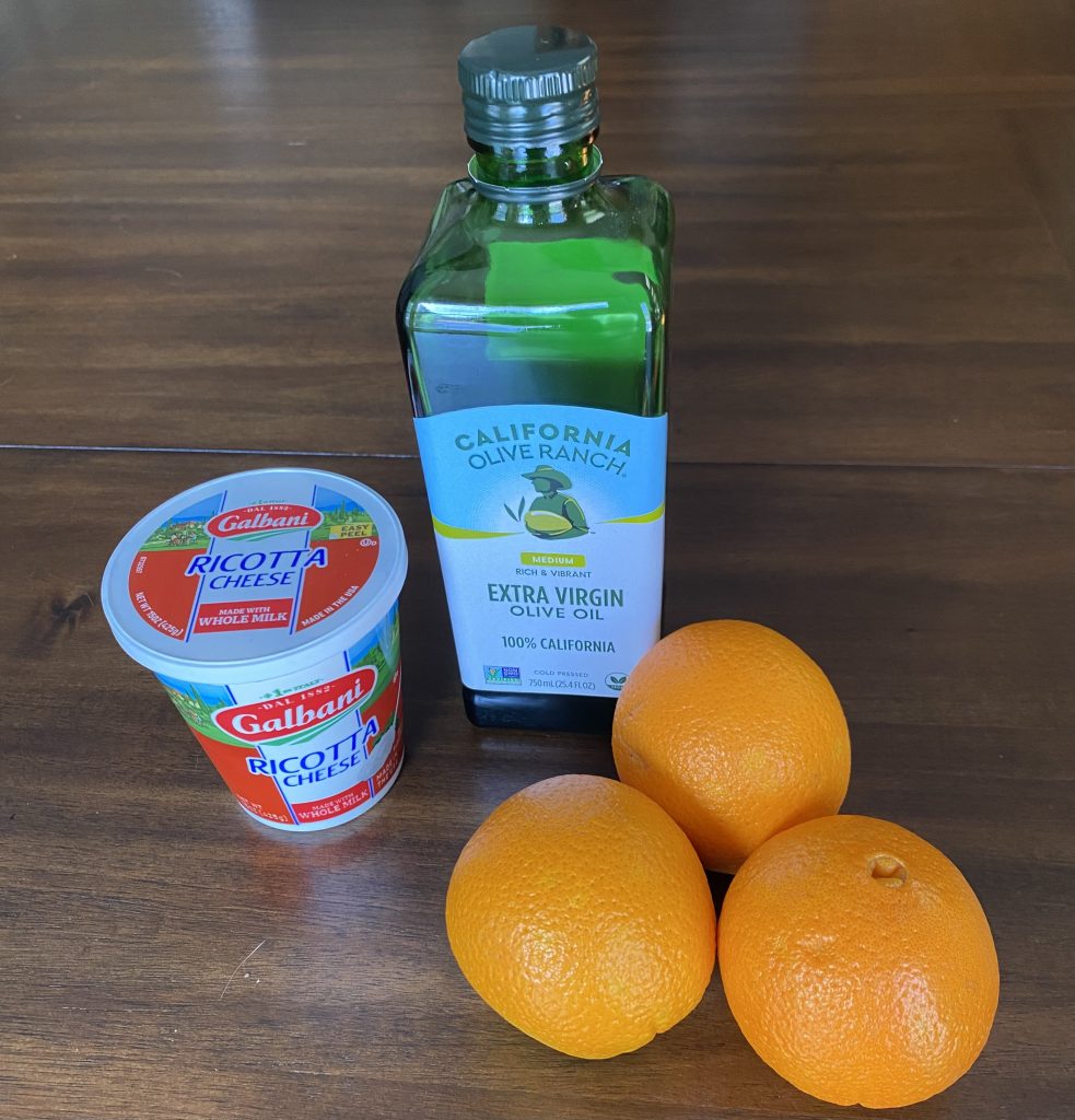 a container of ricotta, a jar of olive oil, and three medium oranges
